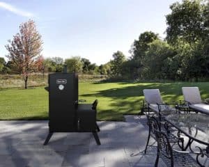 A Dyna-Glo smoker on a terrace with a garden backgroun