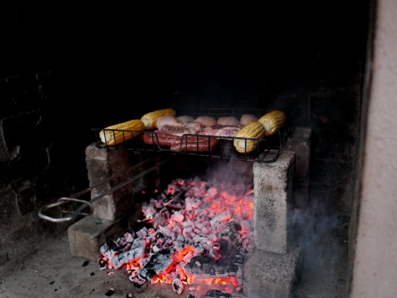 Corn, saussages, and chicken being grilled on charcoal